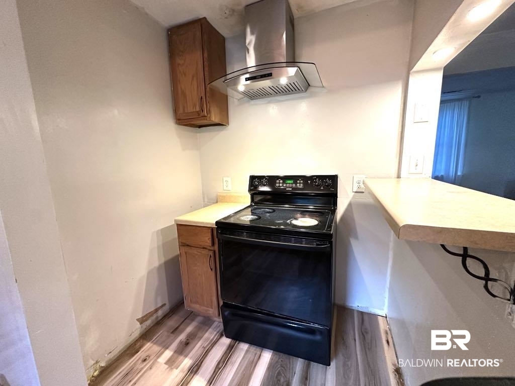 175 Lakeview Loop Daphne, AL 36526 - Photo 5 of 12 Kitchen featuring electric range, wall chimney range hood, light wood-style flooring, and brown cabinets