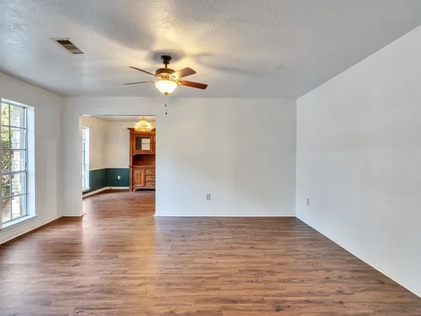 an empty room with wooden floor chandelier fan and windows