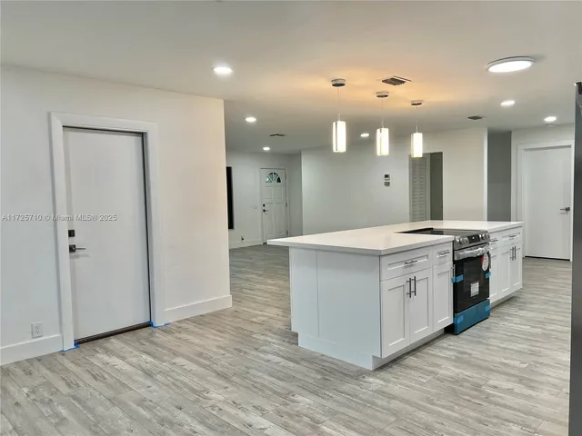 a large white kitchen with a large counter top stainless steel appliances and wooden floor