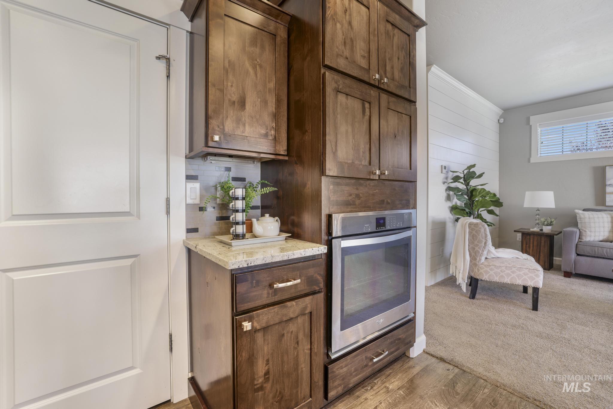 2858 Sunray Loop Twin Falls, ID 83301 - Photo 13 of 45 Kitchen with oven, dark brown cabinets, light wood-style flooring, light stone counters, and decorative backsplash
