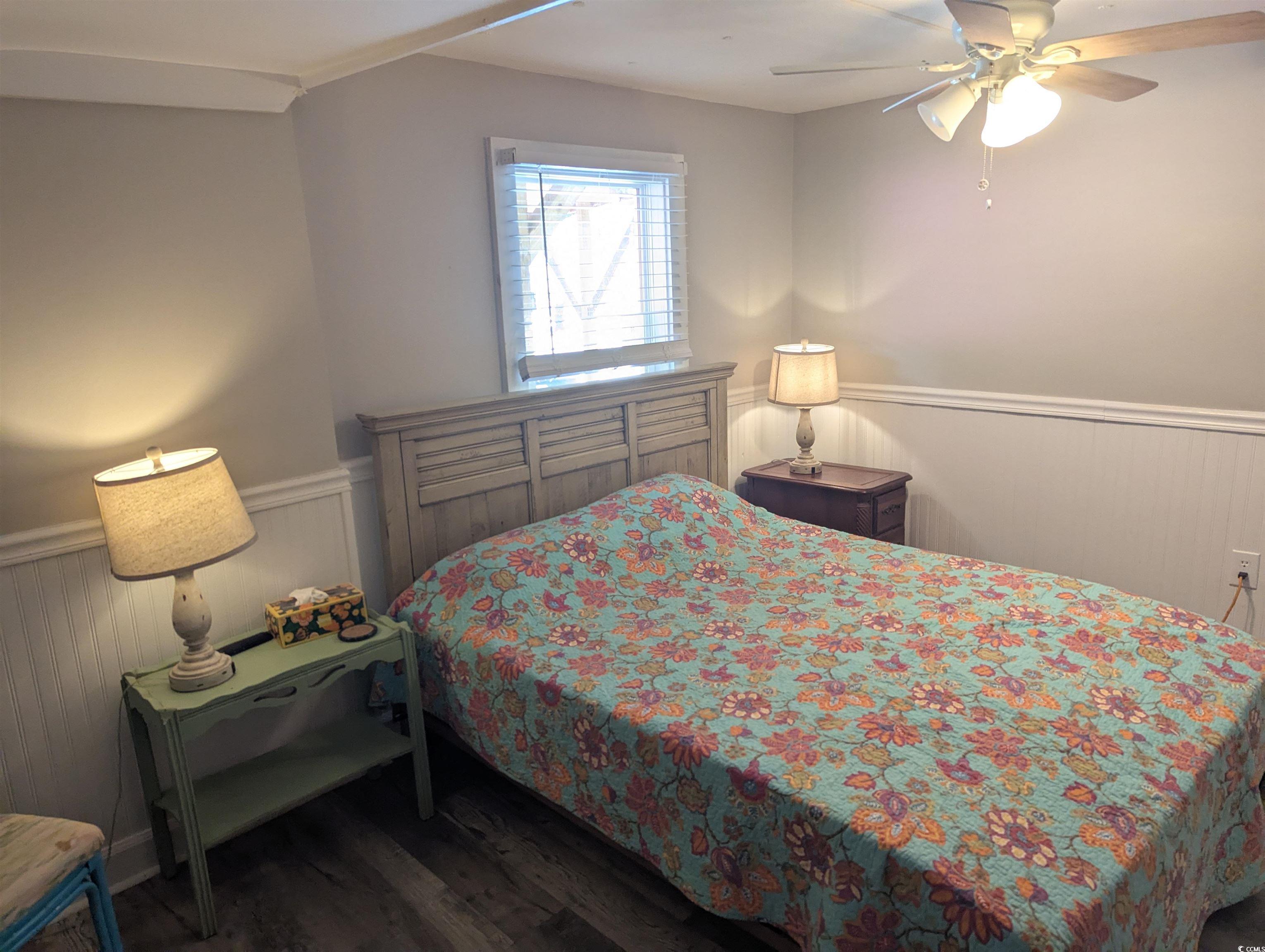 Bedroom with a wainscoted wall, wood finished floors, and a ceiling fan