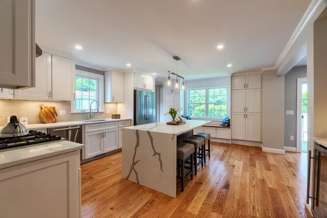 a kitchen with kitchen island granite countertop a stove a sink a refrigerator and white cabinets with wooden floor