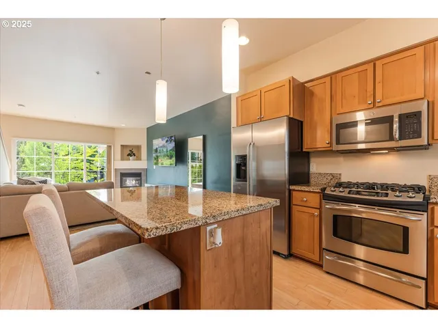 a kitchen with stainless steel appliances granite countertop a refrigerator a stove a sink a dining table and chairs with wooden floor