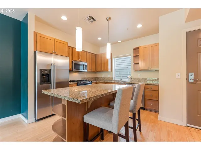 a kitchen with stainless steel appliances granite countertop a table chairs refrigerator and sink