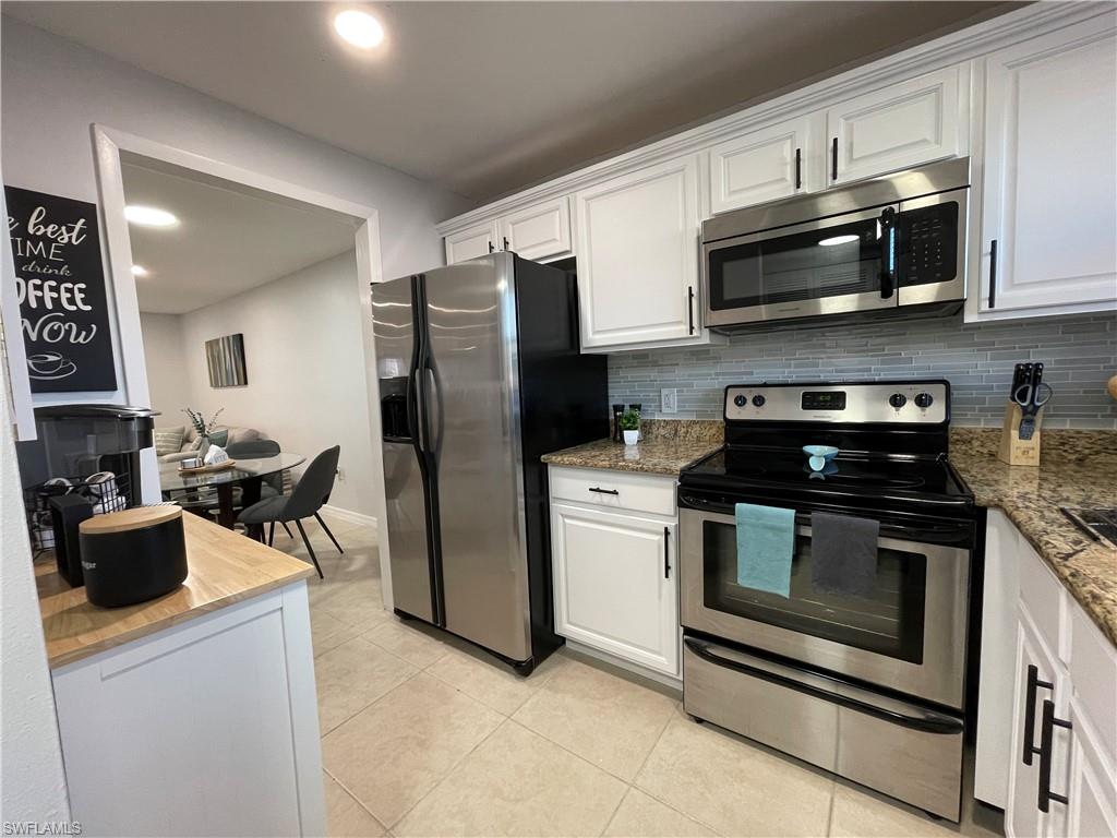 170 Turtle Lake Court, Unit 103 Naples, FL 34105 - Photo 9 of 37 Kitchen with stainless steel appliances, white cabinets, backsplash, light stone counters, and light tile patterned floors
