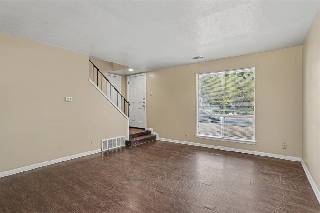 1414 Finley Road Irving, TX 75062 - Photo 3 of 27 Spacious living area featuring wood-finish flooring, a large window, neutral wall tones, and a staircase with a black metal railing