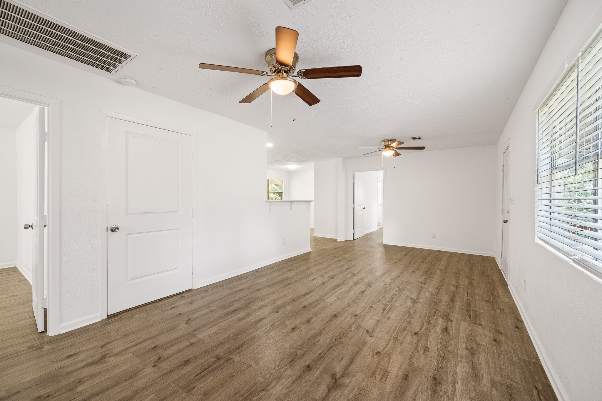61 Hicks Loop West Cleveland, TX 77328 - Photo 13 of 38 Spacious and bright living area featuring elegant wood flooring, ceiling fans, and ample natural light from large windows.