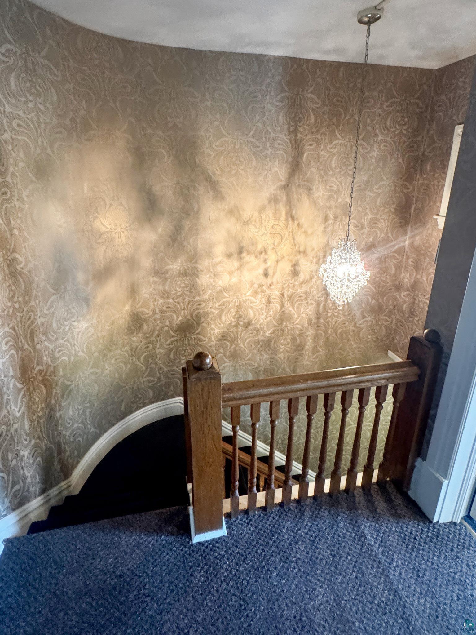 303 East 5th Street Washburn, WI 54891 - Photo 23 of 34 Stairwell featuring ornate patterned wallpaper, a crystal-style pendant light, wood-finish balustrade, and dark carpeting