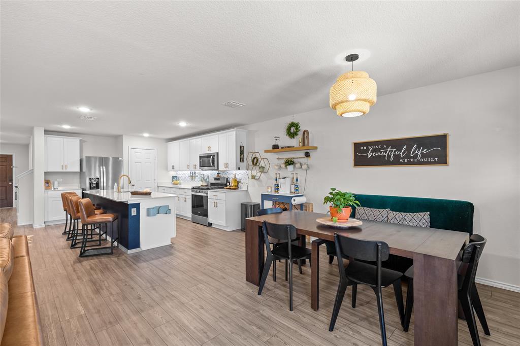 6609 Auburn Dl Road Pilot Point, TX 76258 - Photo 8 of 38 Kitchen and dining area featuring wood-finish flooring, white cabinetry, stainless steel appliances, a center island with seating, and a dining space with a pendant light fixture
