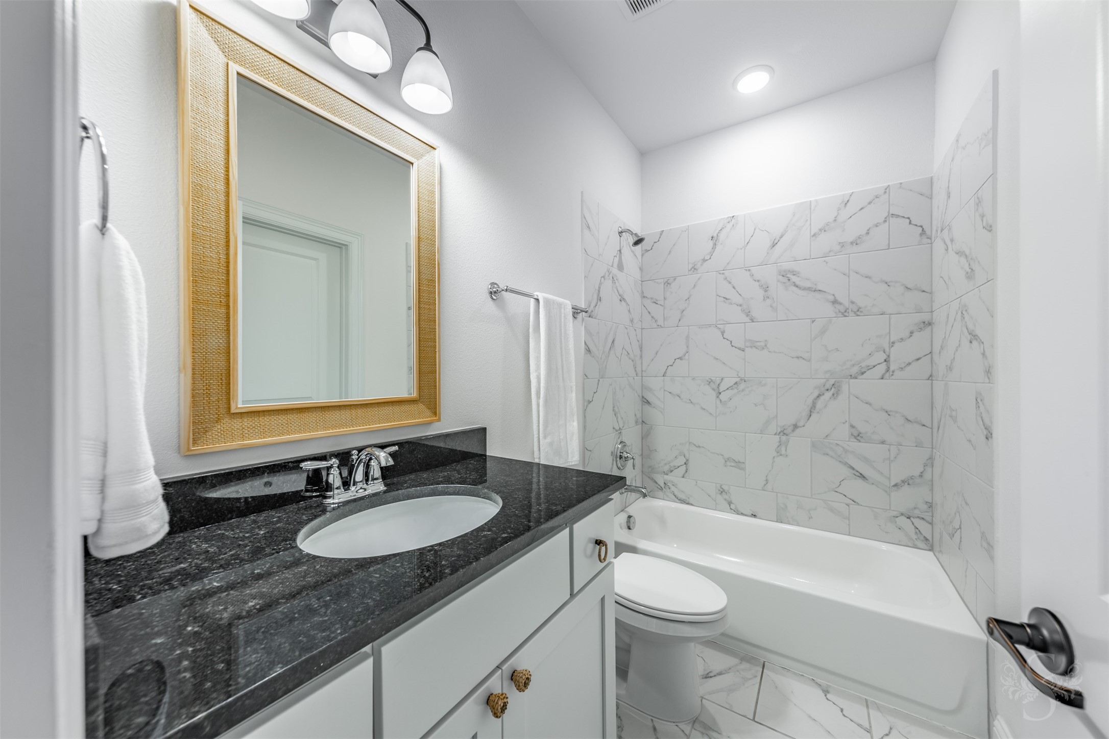 27919 Indigo Ridge Drive Fulshear, TX 77441 - Photo 39 of 50 A beautiful granite countertop and warm framed mirror bring a refined touch to this well-appointed secondary bath. The marble-look tub/shower surround and crisp tile flooring offer durability and style for everyday comfort.