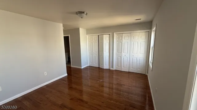 an empty room with wooden floor and windows with curtains