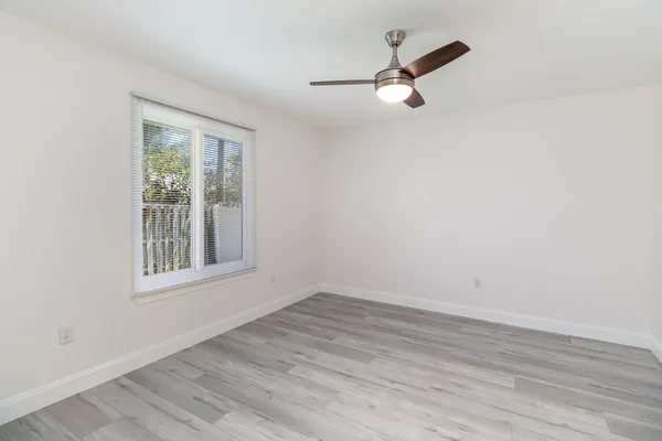 an empty room with wooden floor ceiling fan and windows