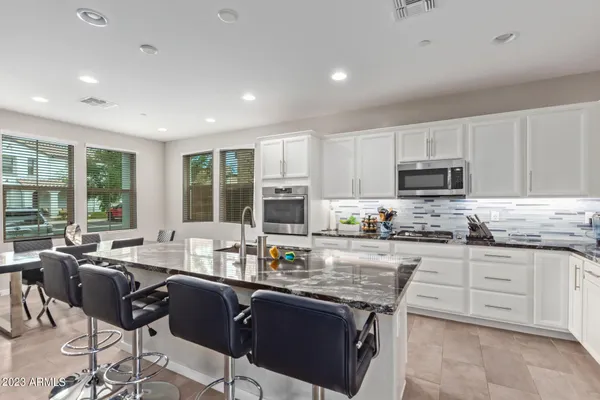 a kitchen with stainless steel appliances granite countertop a stove top oven a sink dishwasher a dining table and chairs with wooden floor