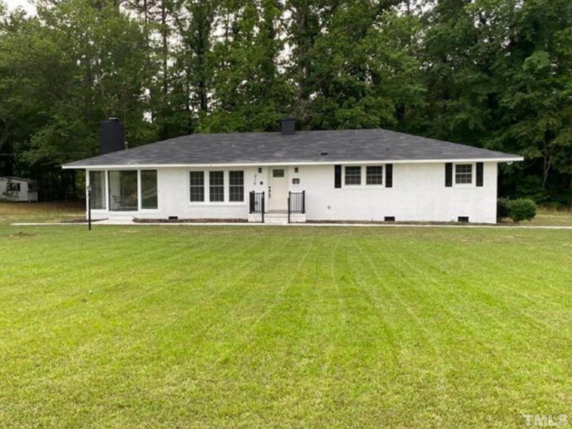 216 Trinity Church Road Louisburg, NC 27549 - Photo 1 of 28 a house that is sitting in the grass with large trees and plants