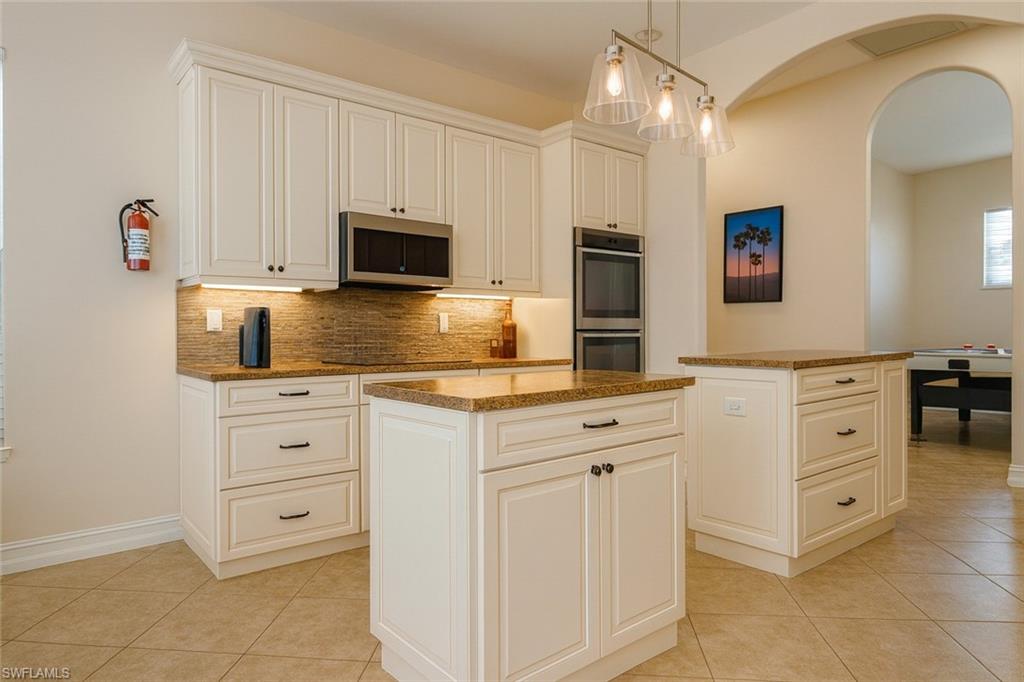 1975 San Marco Road Marco Island, FL 34145 - Photo 10 of 46 Kitchen with a center island, arched walkways, light tile patterned flooring, decorative backsplash, and decorative light fixtures