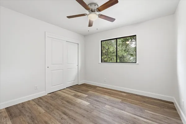 an empty room with wooden floor ceiling fan and windows