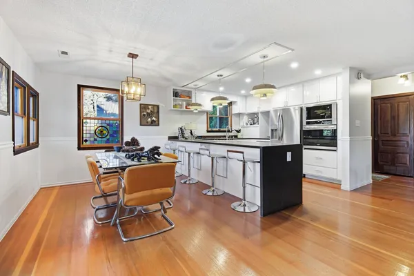 a kitchen with stainless steel appliances granite countertop a stove top oven a refrigerator a dining table and chairs with wooden floor