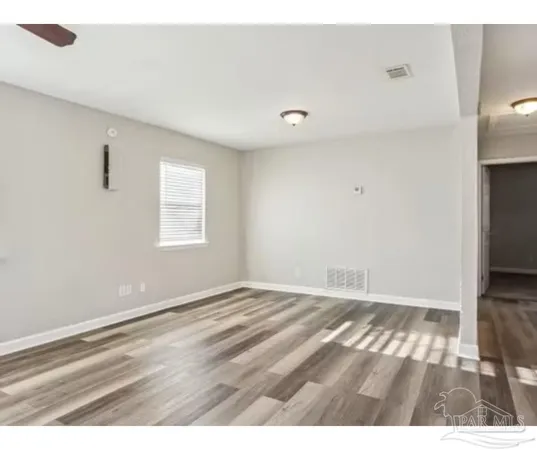 a view of an empty room with wooden floor and a window