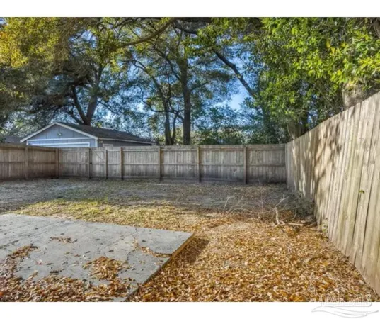 a view of a backyard with large trees and wooden fence