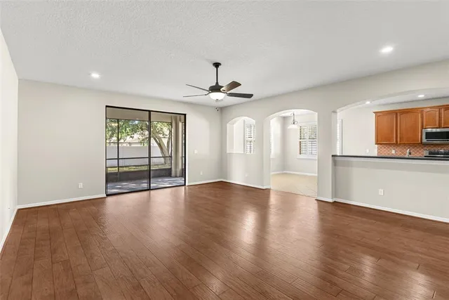 a view of an empty room with wooden floor and a kitchen