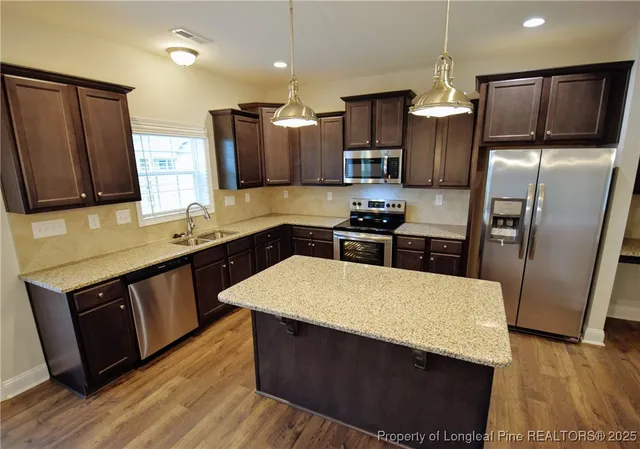 a kitchen with granite countertop a refrigerator a sink dishwasher and wooden cabinets with wooden floor
