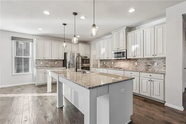 a kitchen with stainless steel appliances granite countertop a sink a stove a refrigerator cabinets and wooden floor