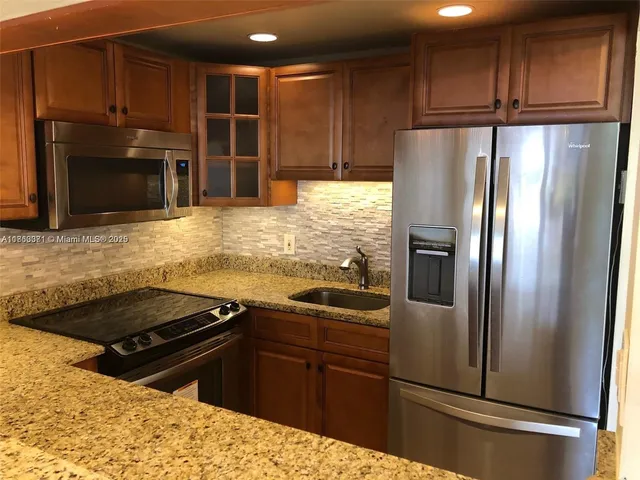 a kitchen with granite countertop a refrigerator stove and cabinets
