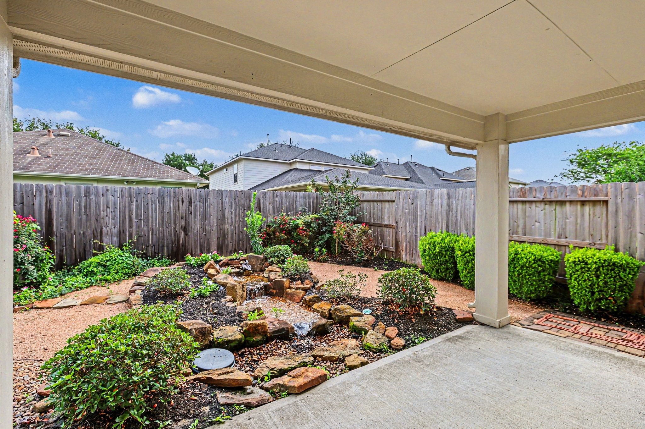 25222 Ginger Ranch Drive Katy, TX 77494 - Photo 30 of 33 Charming backyard with a covered patio, well-maintained garden, and a small rock waterfall feature, providing a serene outdoor space perfect for relaxation.