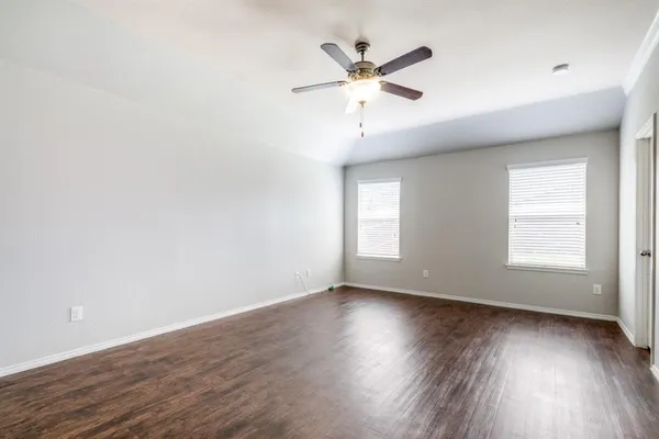 an empty room with wooden floor fan and windows