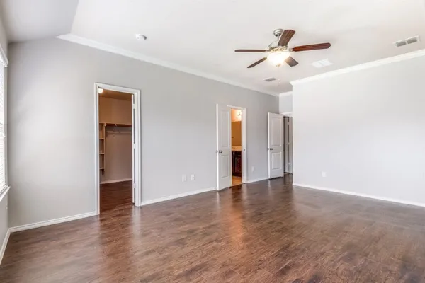 a view of an empty room with wooden floor and a ceiling fan