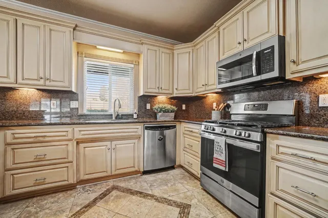 a kitchen with granite countertop white cabinets stainless steel appliances and a window