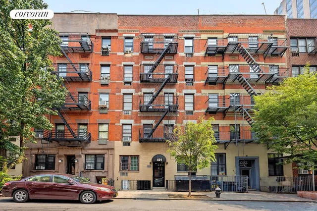 a front view of a building with lot of cars and trees