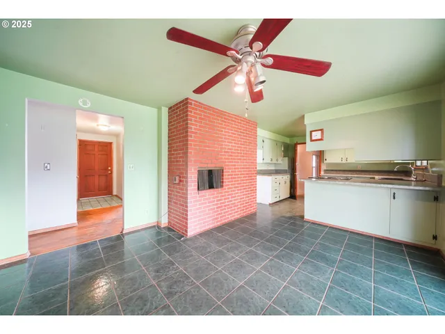a view of an empty room and kitchen with a ceiling fan