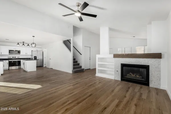 a view of a livingroom with a fireplace a ceiling fan and a kitchen view