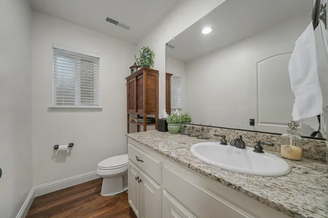 a bathroom with a granite countertop double vanity sink a mirror and a toilet