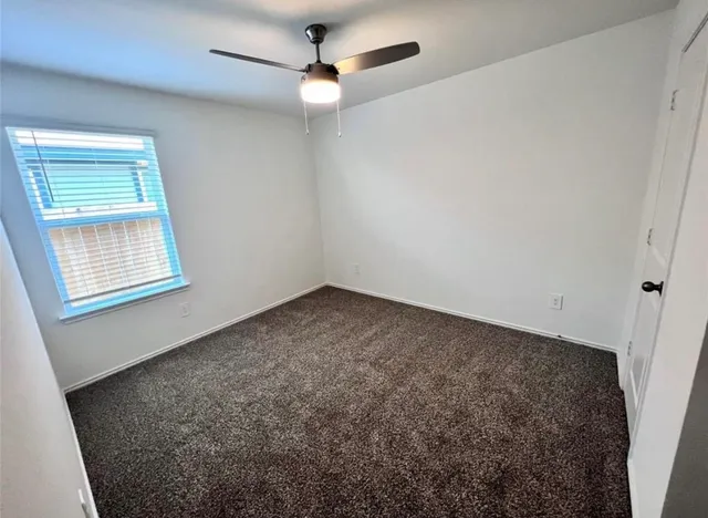 an empty room with a chandelier fan and windows