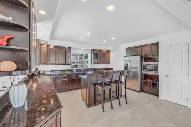 a kitchen with stainless steel appliances kitchen island granite countertop a stove a refrigerator a sink a dining table and chairs with wooden floor