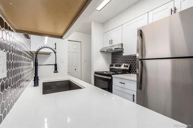 a kitchen with granite countertop a refrigerator sink stove and white cabinets