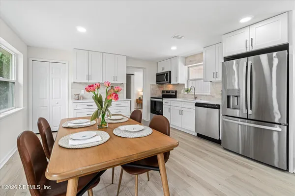 a kitchen with stainless steel appliances granite countertop a dining table chairs refrigerator and microwave