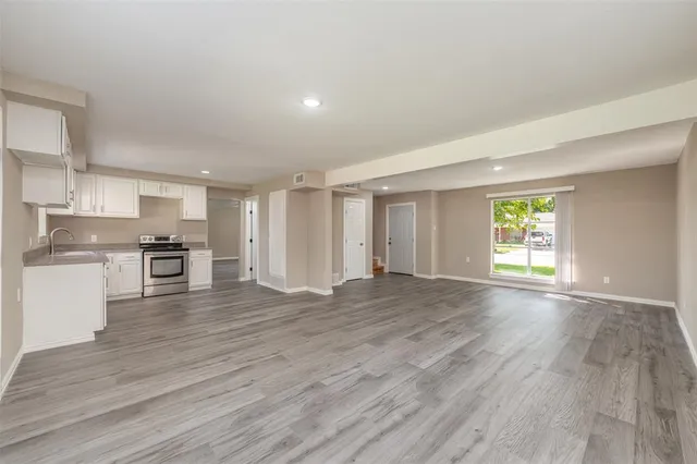 a view of empty room with wooden floor and kitchen