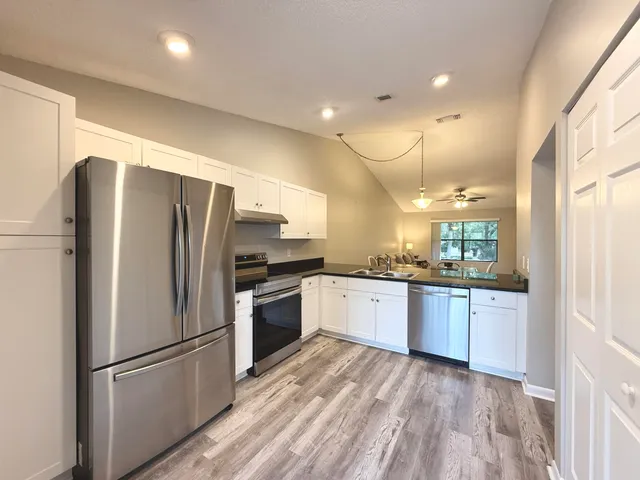 a kitchen with granite countertop stainless steel appliances a refrigerator a sink and white cabinets