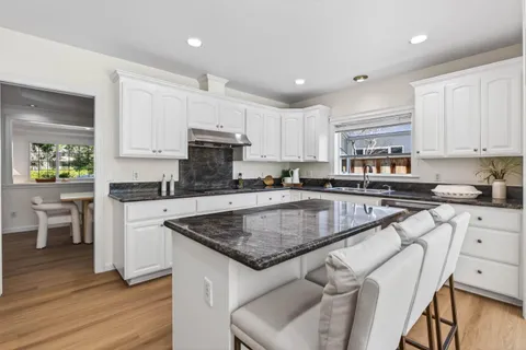 a kitchen with stainless steel appliances granite countertop a stove a sink dishwasher a microwave oven and a dining table with wooden floor
