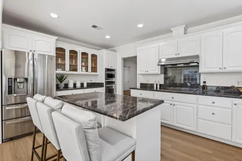 a kitchen with stainless steel appliances granite countertop a stove top oven a sink a dining table and chairs