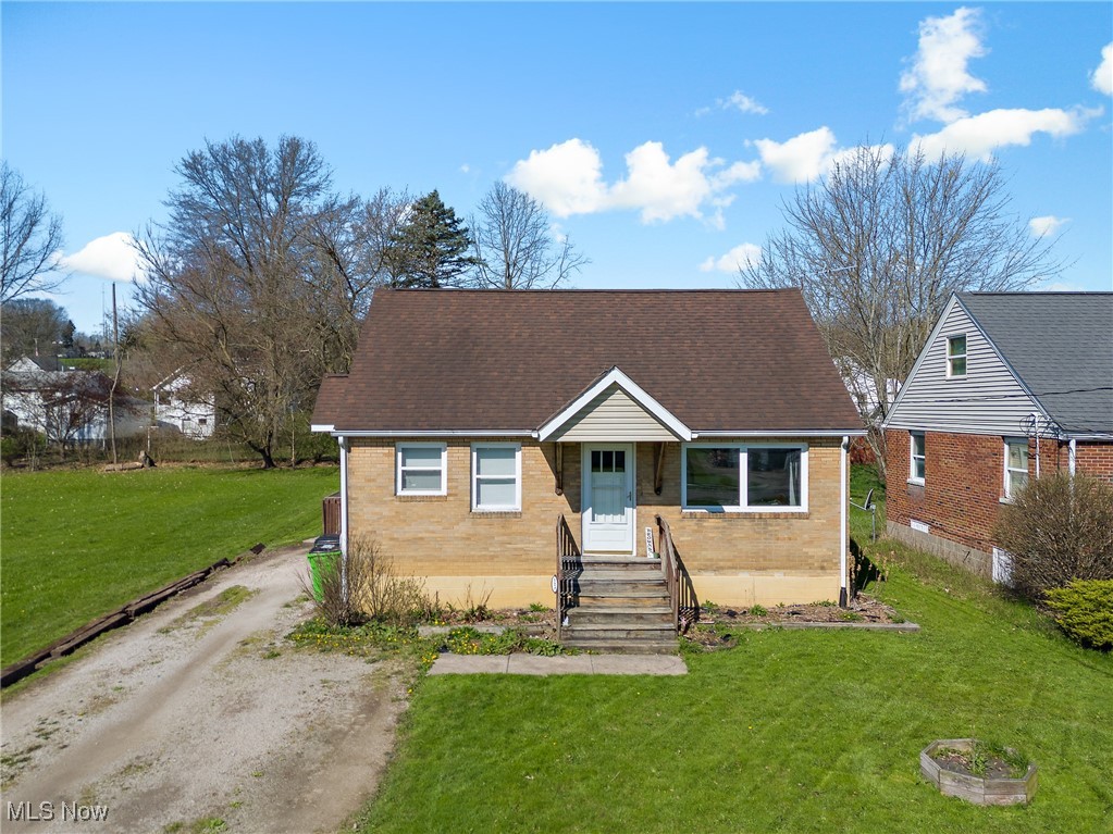 Cape cod-style house with brick siding, dirt driveway, roof with shingles, and a front yard