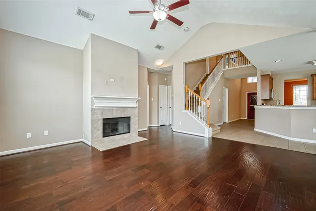 a view of a livingroom with wooden floor a ceiling fan a fireplace and windows
