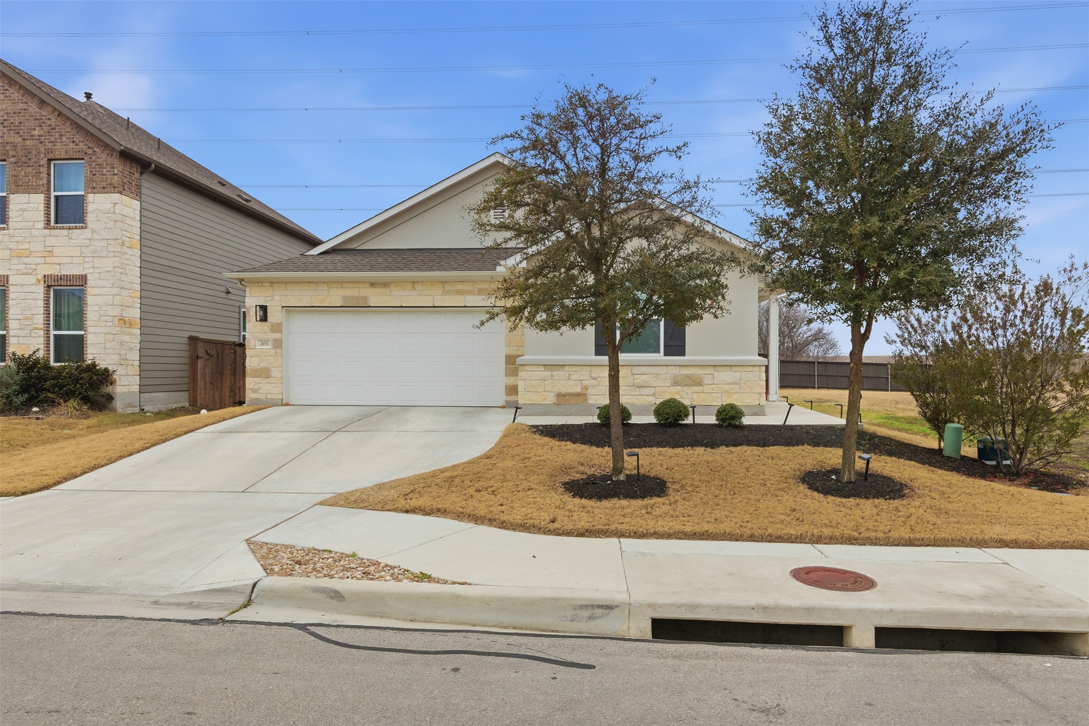 View of front facade featuring driveway, stone siding, and an attached garage