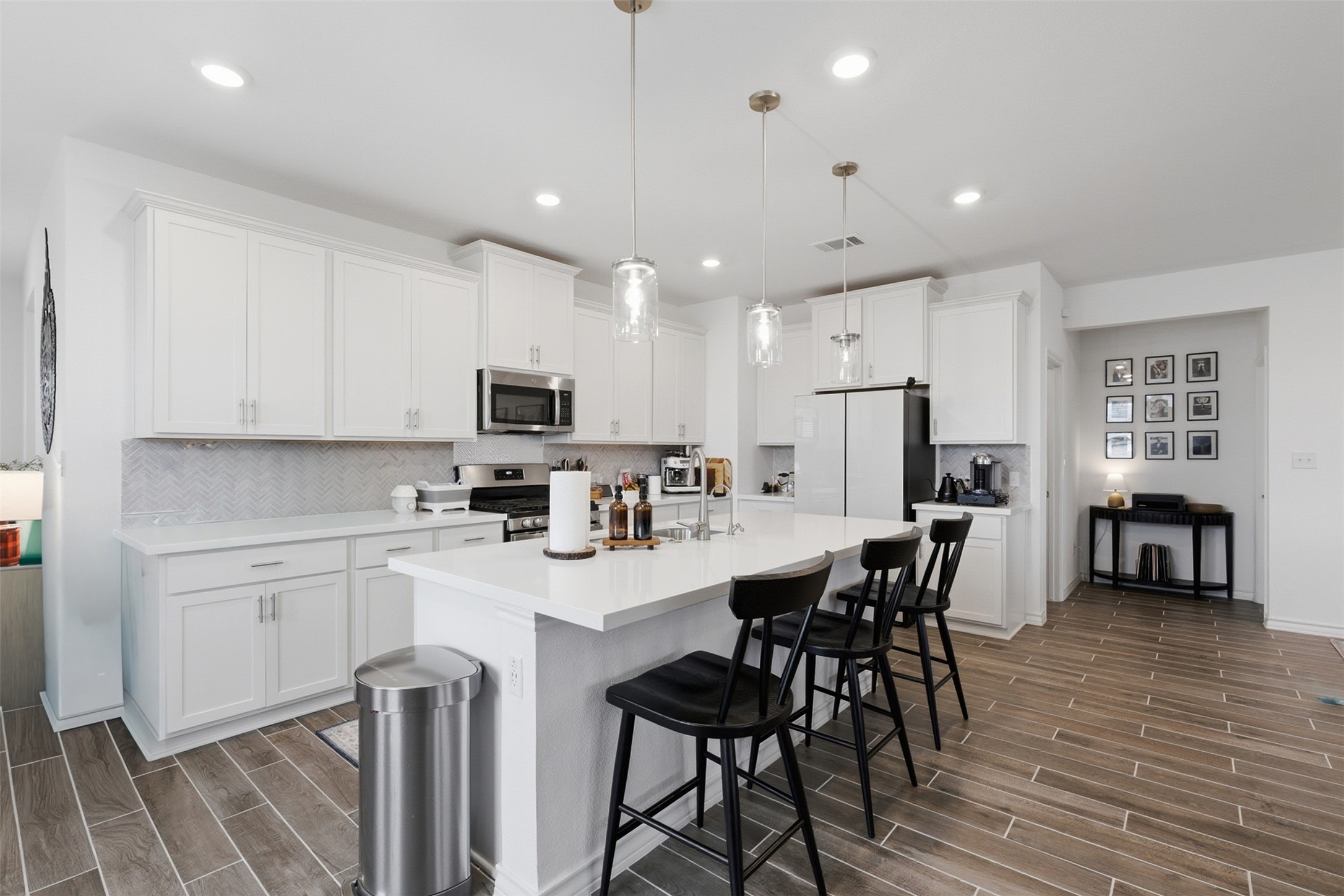 203 Stinchcomb Road Hutto, TX 78634 - Photo 13 of 30 Kitchen with wood finish floors, light countertops, a kitchen breakfast bar, decorative light fixtures, and a kitchen island with sink