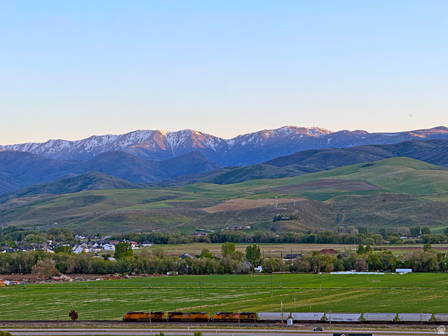 851 Grandview Drive Morgan, UT 84050 - Photo 12 of 68 Expansive landscape featuring snow-capped mountains, verdant rolling hills, a distant town, and a railway track with a passing train