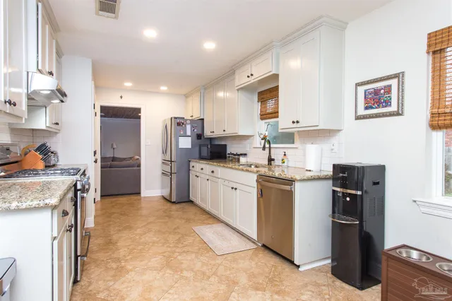 a kitchen with stainless steel appliances granite countertop a stove top oven a sink a refrigerator and white cabinets with wooden floor