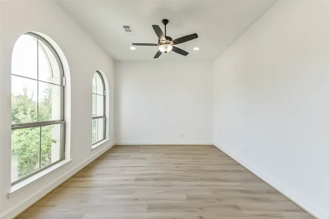 an empty room with wooden floor fan and windows